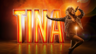 Tina Turner står foran et stort lysende skilt, hvor der står TINA på. Hun har en mikrofon i hånden.